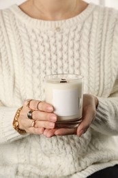 Woman with stylish jewelry holding burning soy candle, closeup