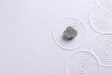 Photo of Zen garden stones on white sand with pattern, top view. Space for text