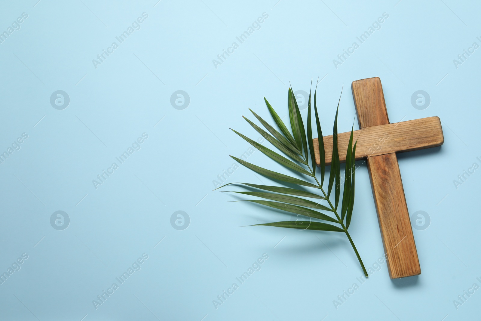 Photo of Wooden cross and palm leaf on light blue background, top view with space for text. Easter attributes
