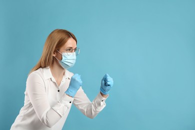Photo of Woman with protective mask and gloves in fighting pose on light blue background, space for text. Strong immunity concept