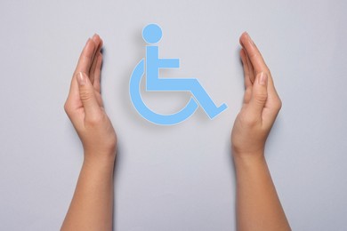 Disability inclusion. Woman protecting wheelchair symbol on light background, closeup