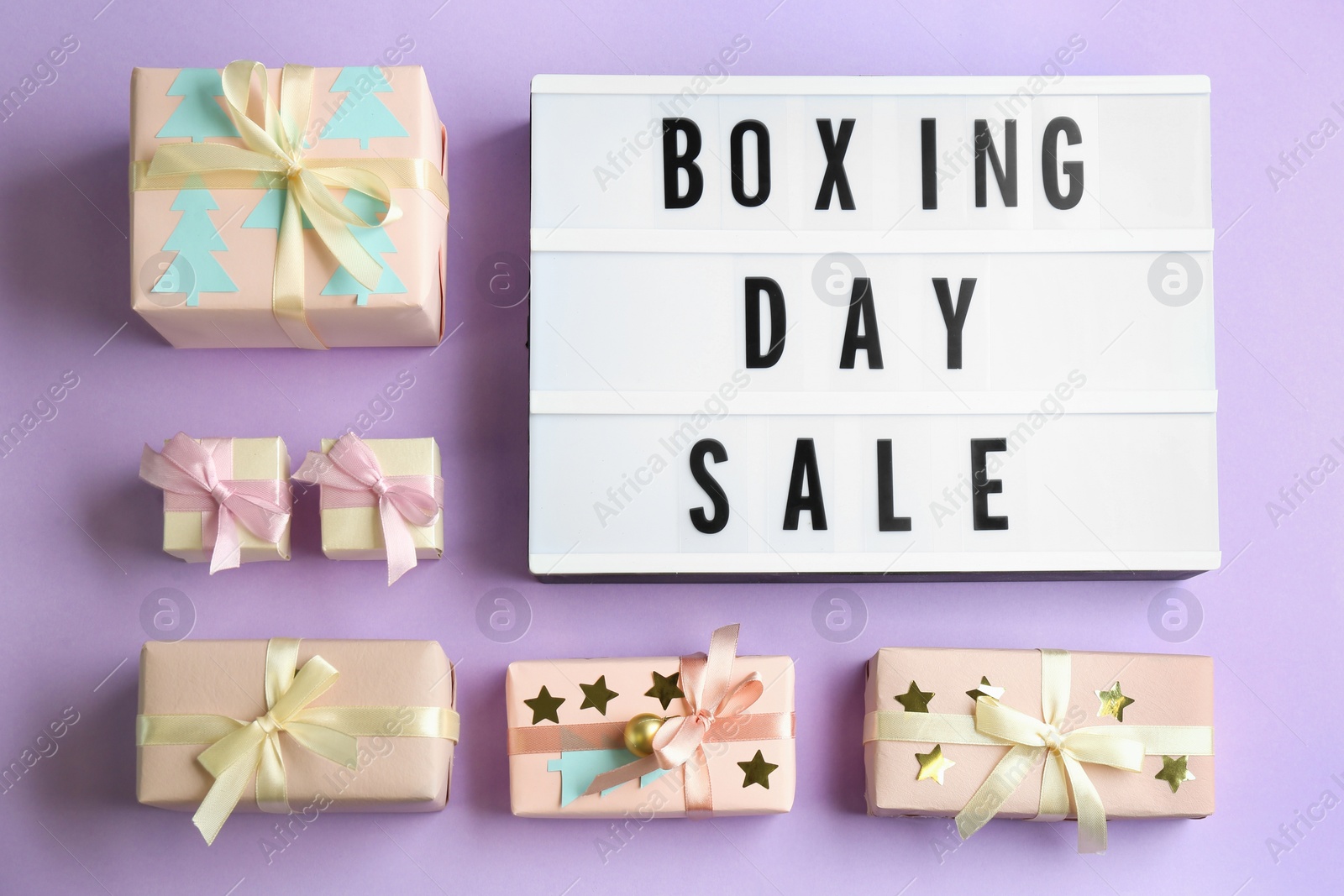 Photo of Lightbox with phrase BOXING DAY SALE and Christmas decorations on lilac background, flat lay