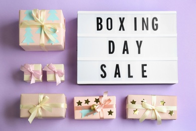 Lightbox with phrase BOXING DAY SALE and Christmas decorations on lilac background, flat lay