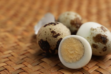 Unpeeled and peeled hard boiled quail eggs on wicker surface, closeup