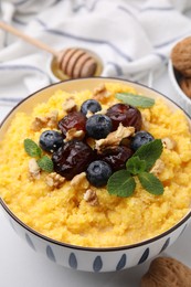 Photo of Tasty cornmeal with blueberries, dates, walnuts and mint in bowl on table, closeup