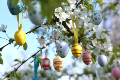 Photo of Beautifully painted Easter eggs hanging on blooming tree outdoors, closeup