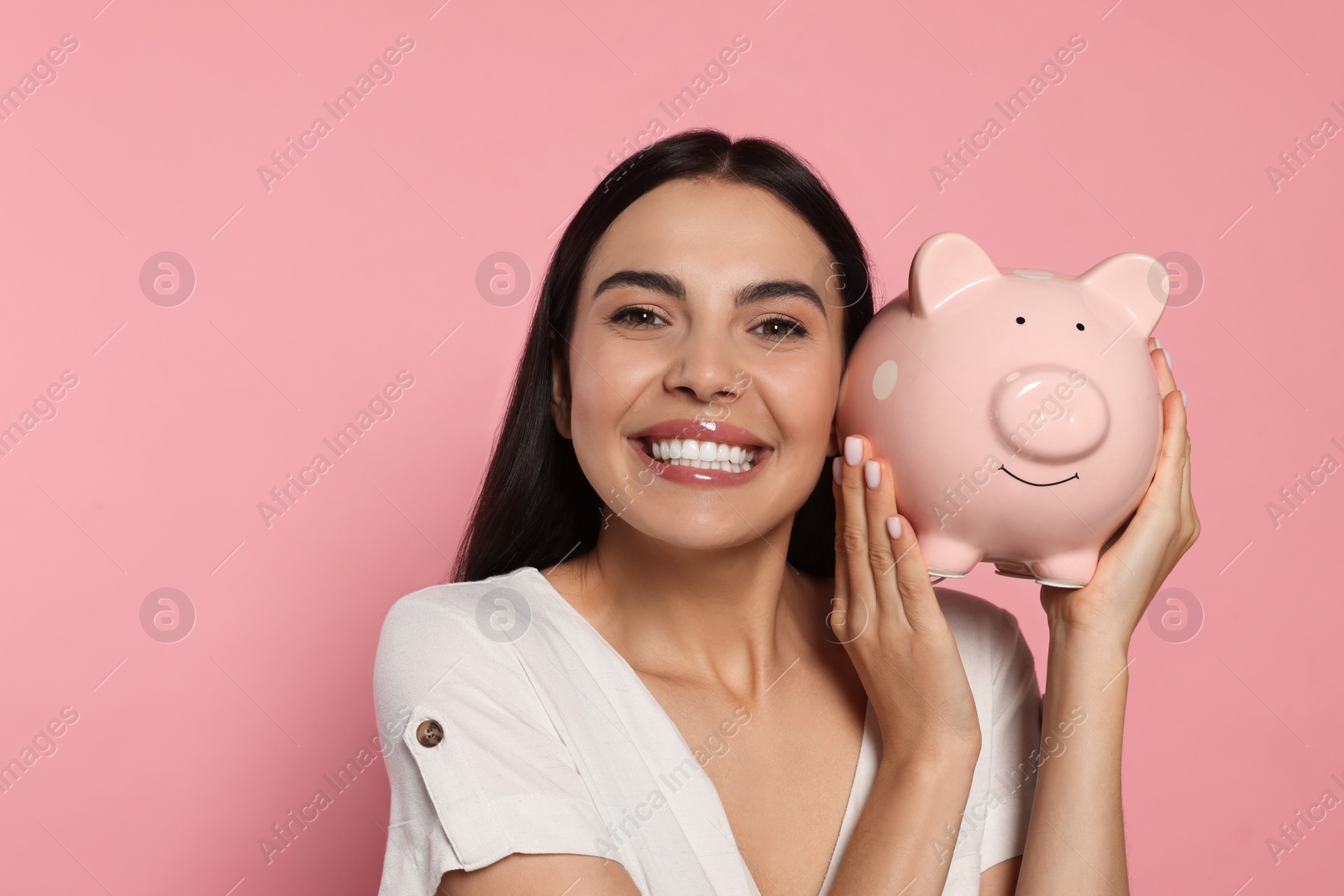 Photo of Emotional young woman with ceramic piggy bank on pale pink background