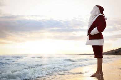 Photo of Santa Claus on beach, space for text. Christmas vacation