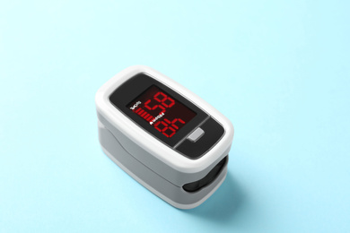 Photo of Modern fingertip pulse oximeter on light blue background, closeup