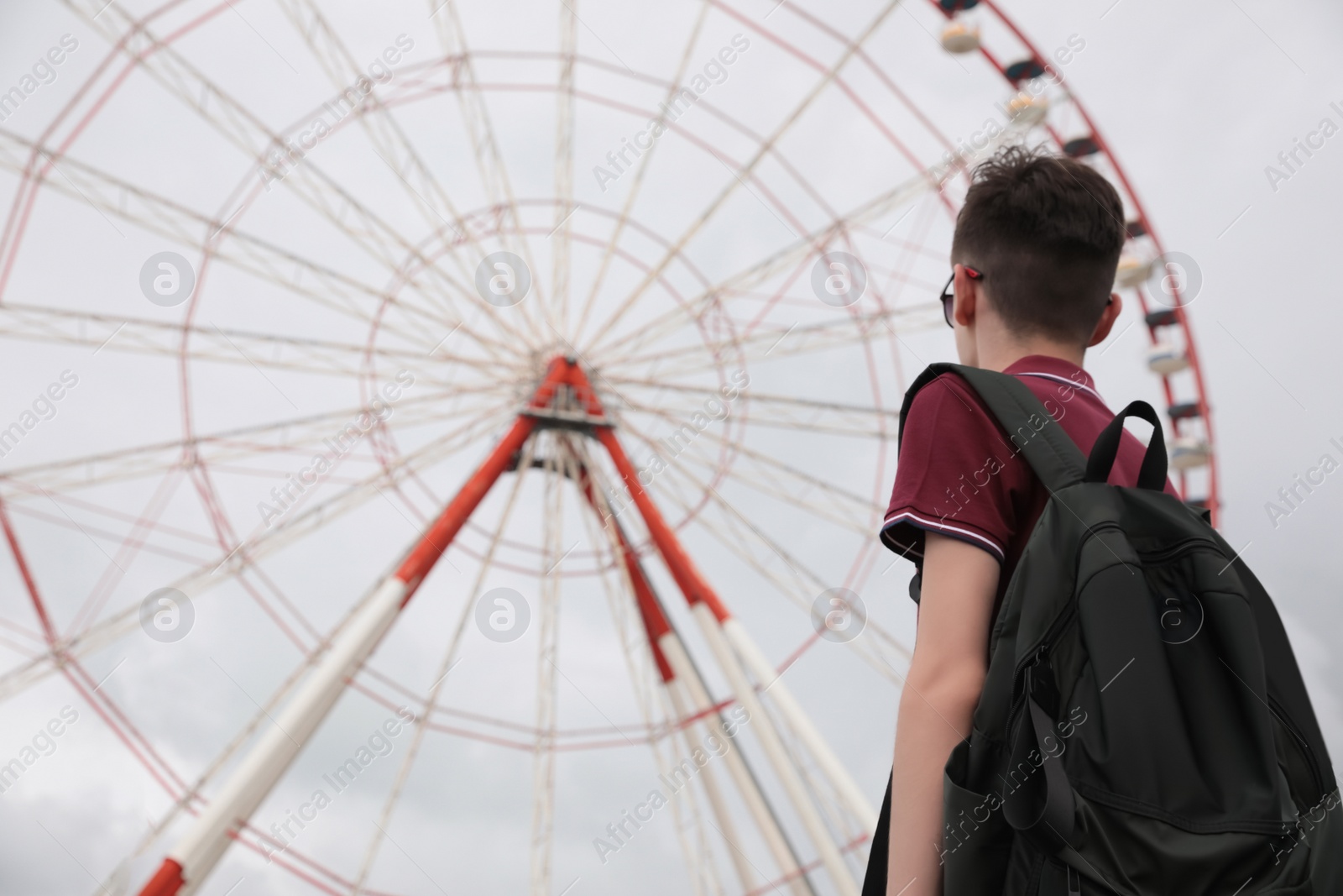 Photo of Teenage boy near large Ferris wheel outdoors, back view. Space for text