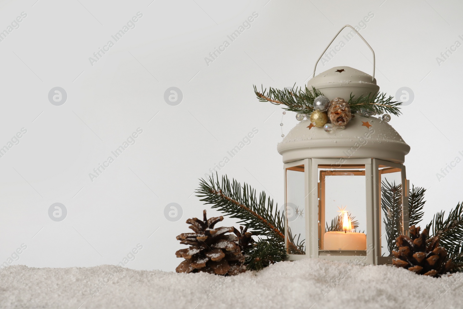 Photo of Decorative lantern and Christmas decor on snow against light grey background. Space for text