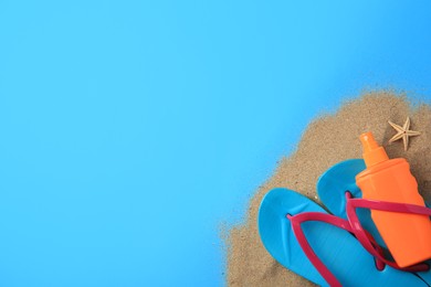 Photo of Flip flops, sunscreen and sand on light blue background, flat lay with space for text. Beach accessories