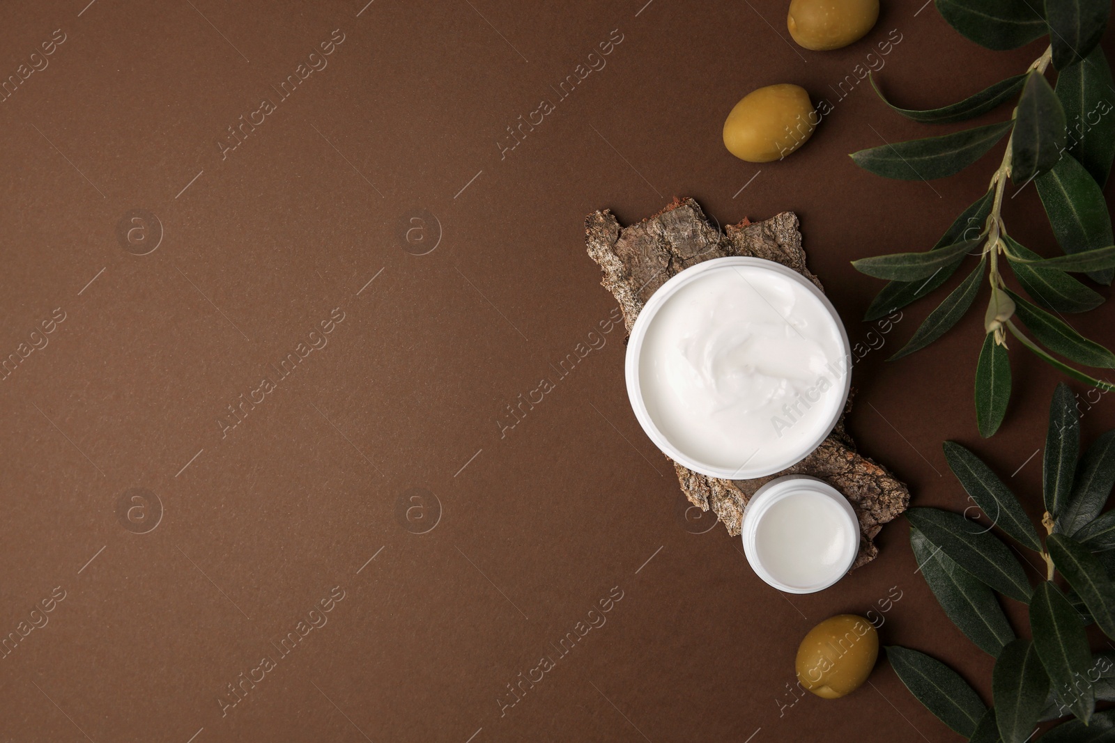 Photo of Flat lay composition with jars of cream and olives on brown background. Space for text