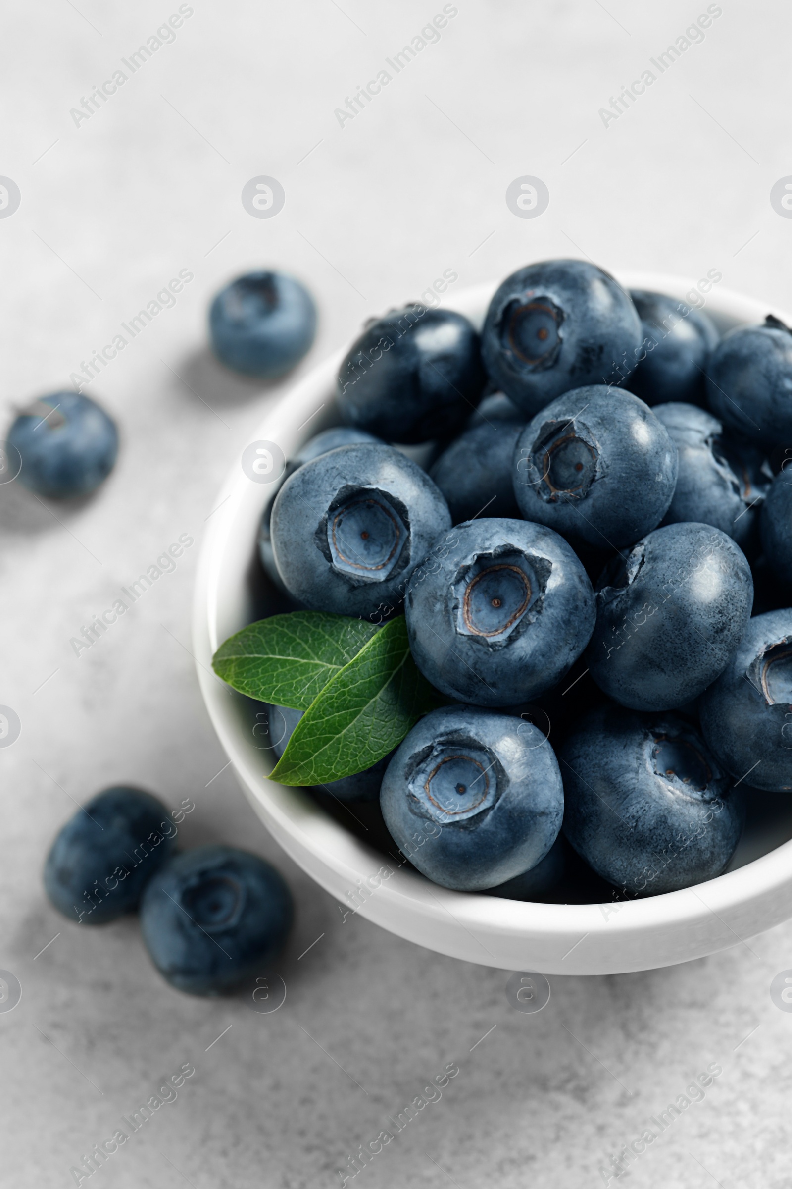 Photo of Bowl of fresh tasty blueberries on light grey table, closeup