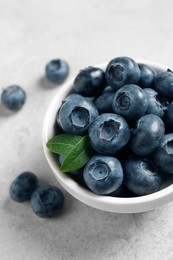 Photo of Bowl of fresh tasty blueberries on light grey table, closeup