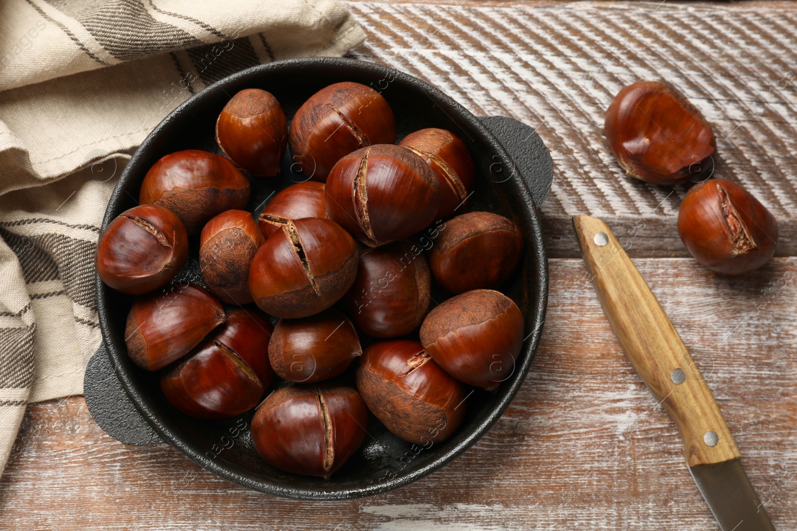 Photo of Fresh edible sweet chestnuts in frying pan on wooden table, flat lay