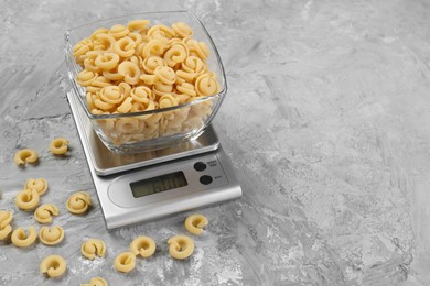 Photo of Kitchen scale with bowl of pasta on grey textured table. Space for text