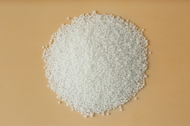 Photo of Pellets of ammonium nitrate on beige background, flat lay. Mineral fertilizer