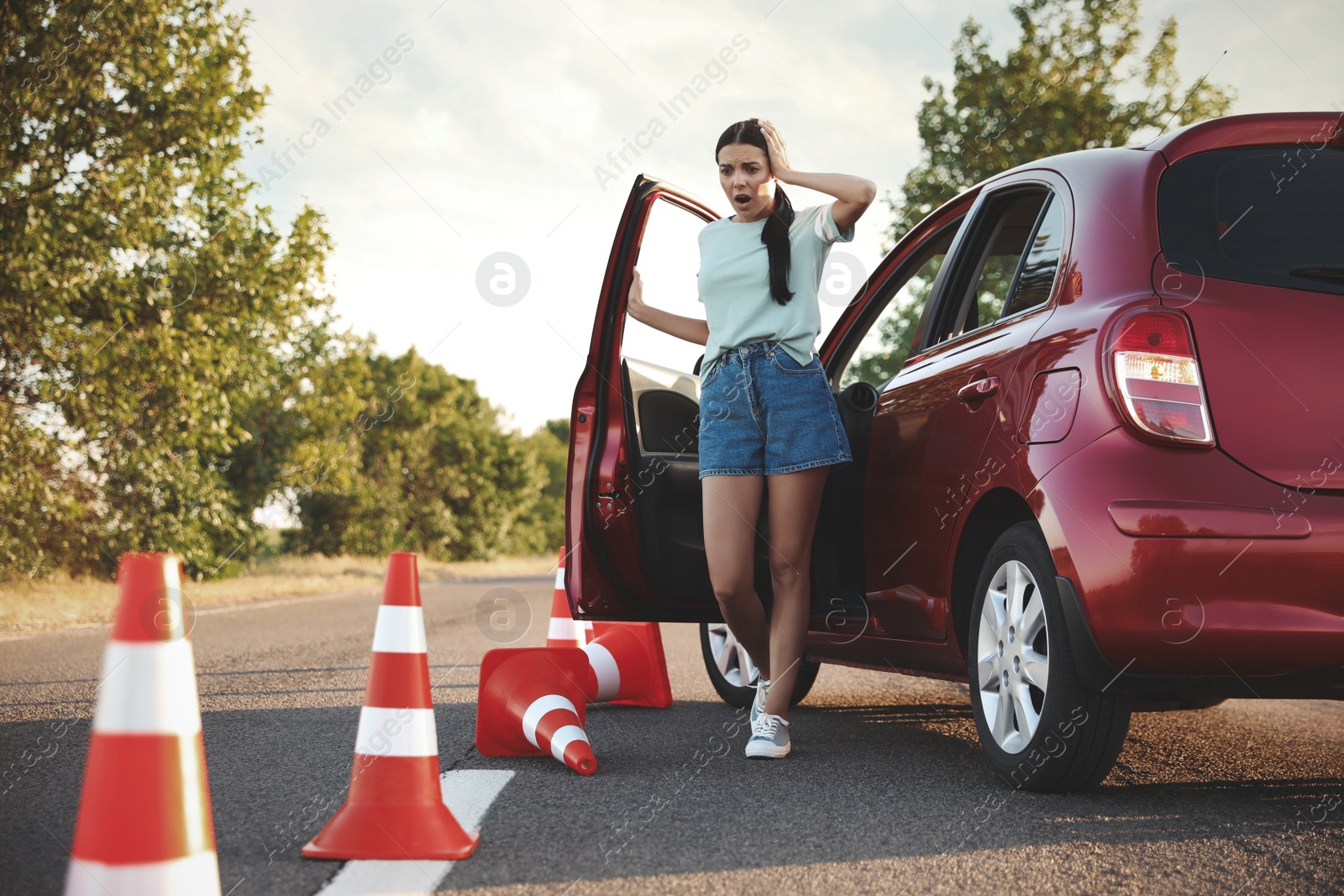 Photo of Stressed young woman in car near fallen traffic cones outdoors. Failed driving school exam