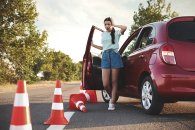 Stressed young woman in car near fallen traffic cones outdoors. Failed driving school exam