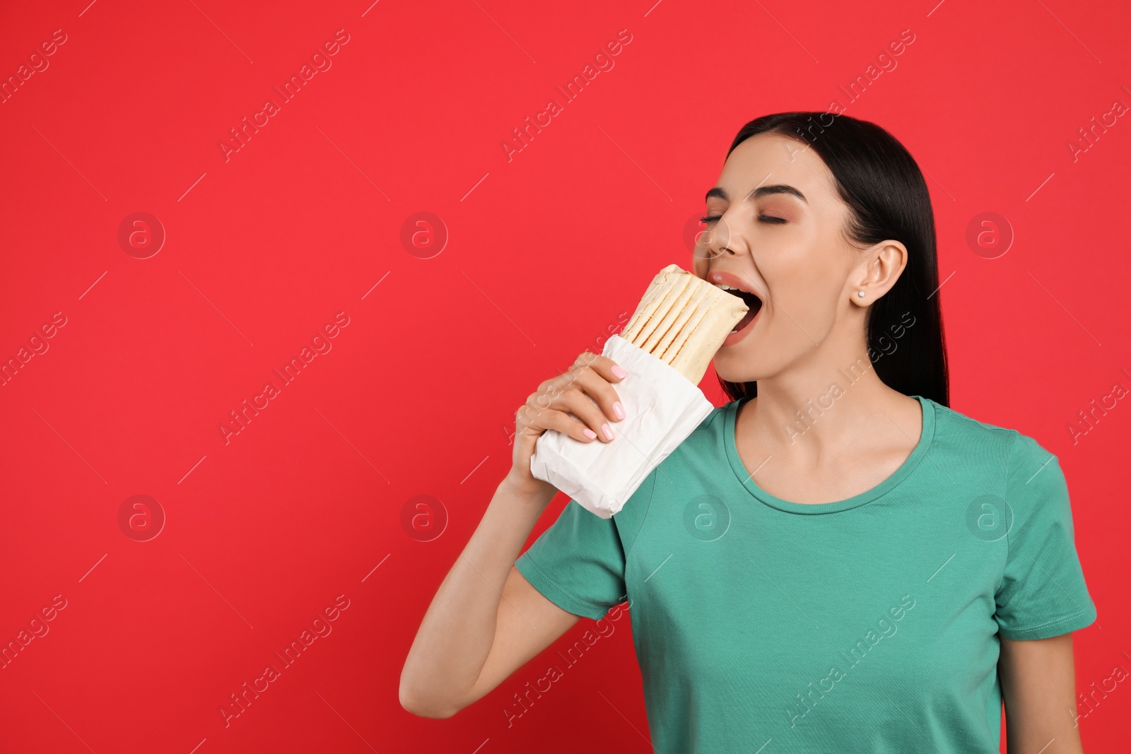 Photo of Young woman eating delicious shawarma on red background. Space for text