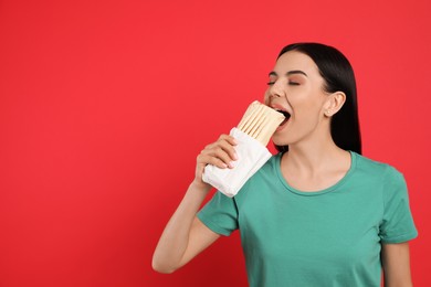 Photo of Young woman eating delicious shawarma on red background. Space for text