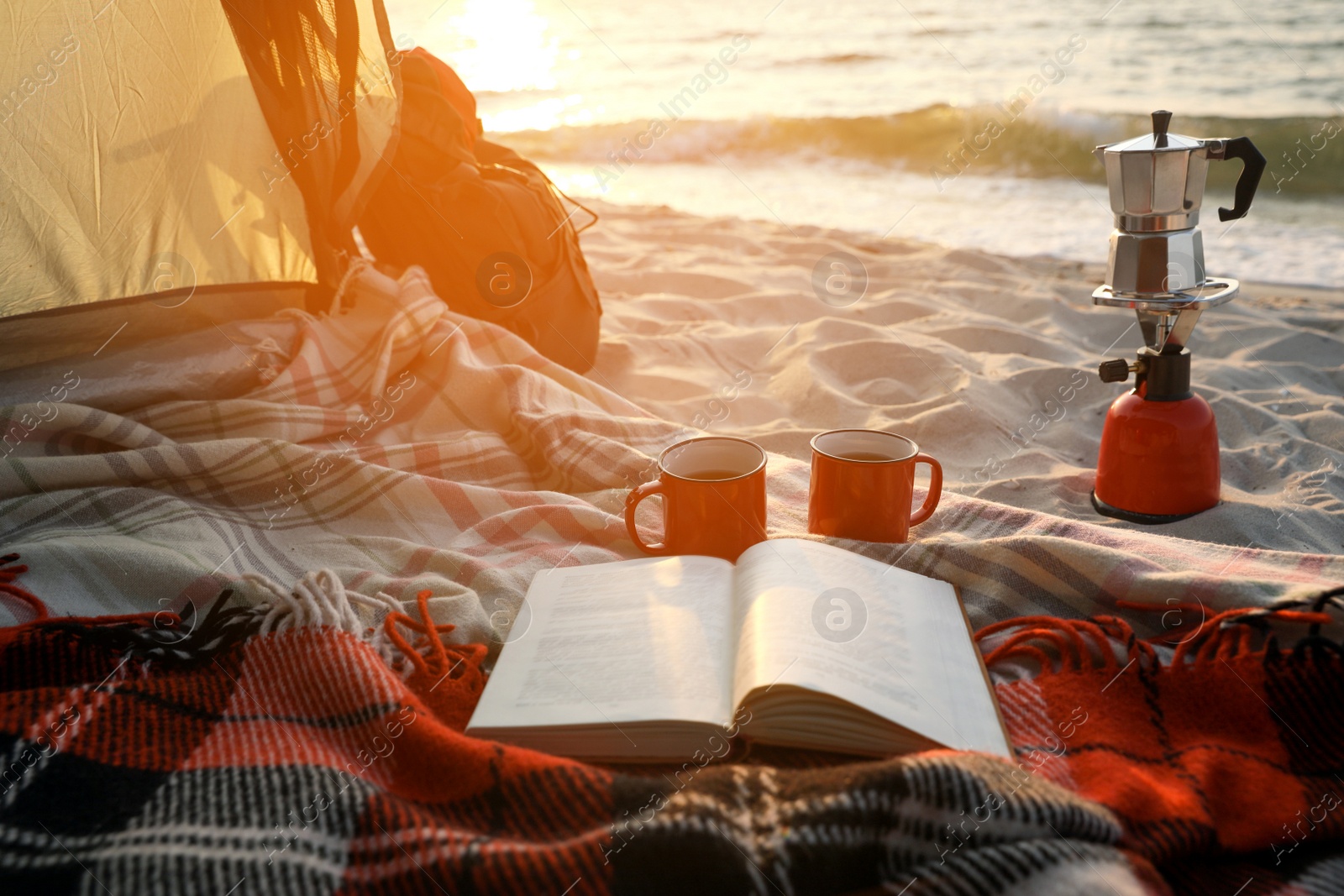 Photo of Cups, book on blanket and backpack in camping tent. View from inside