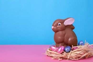 Photo of Chocolate Easter bunny and eggs on pink table against light blue background. Space for text