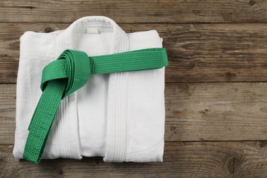 Photo of Green karate belt and white kimono on wooden background, top view. Space for text