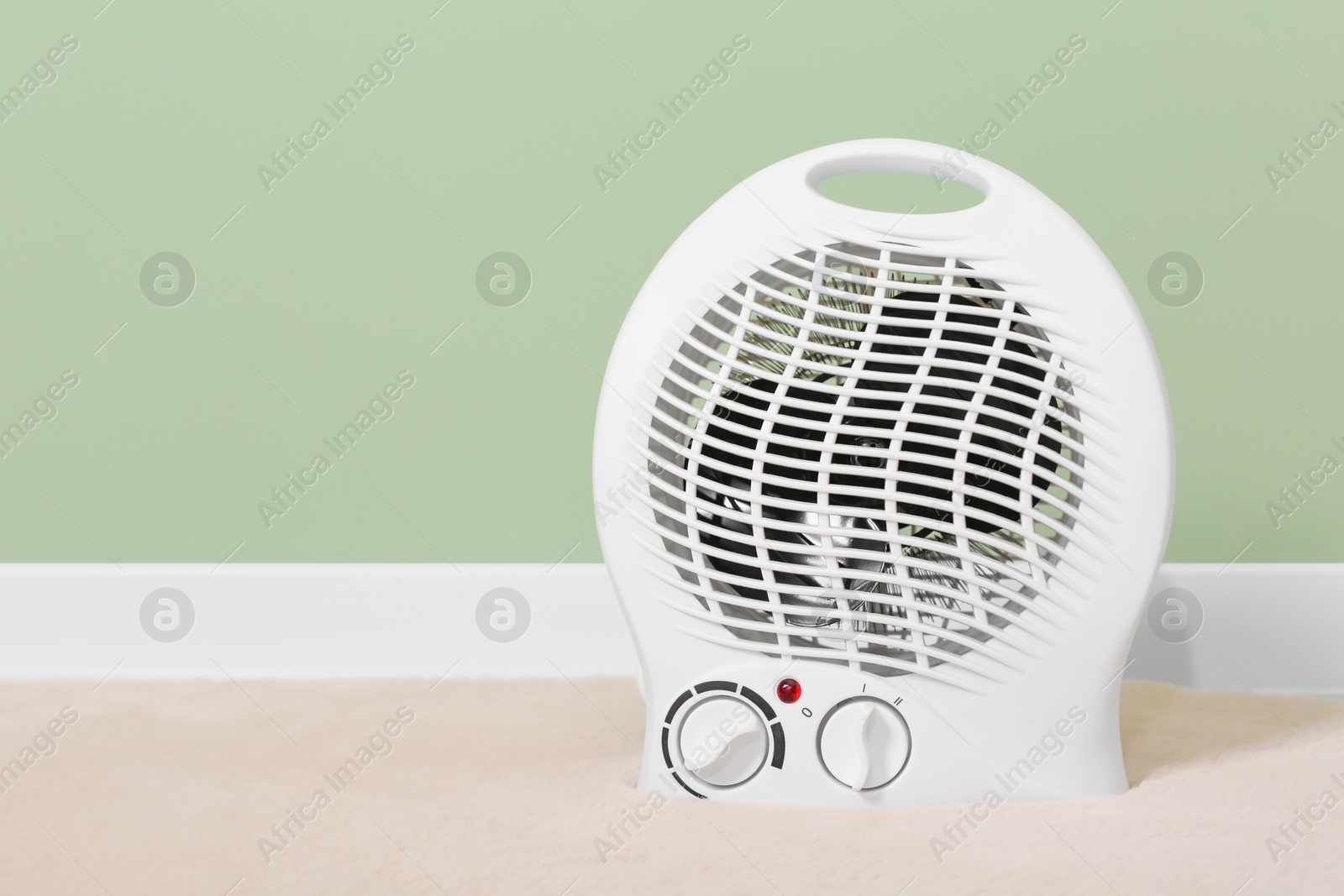 Photo of Electric fan heater near pale green wall indoors. Space for text