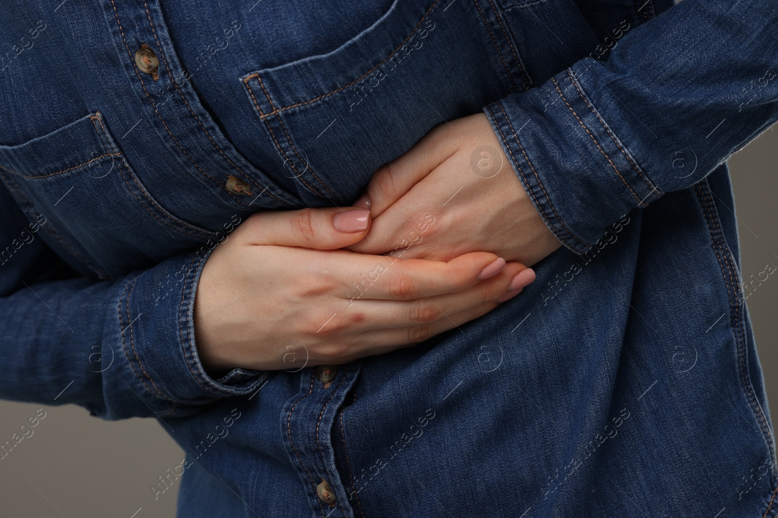 Photo of Woman suffering from stomach pain on grey background, closeup