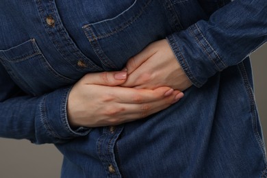 Photo of Woman suffering from stomach pain on grey background, closeup