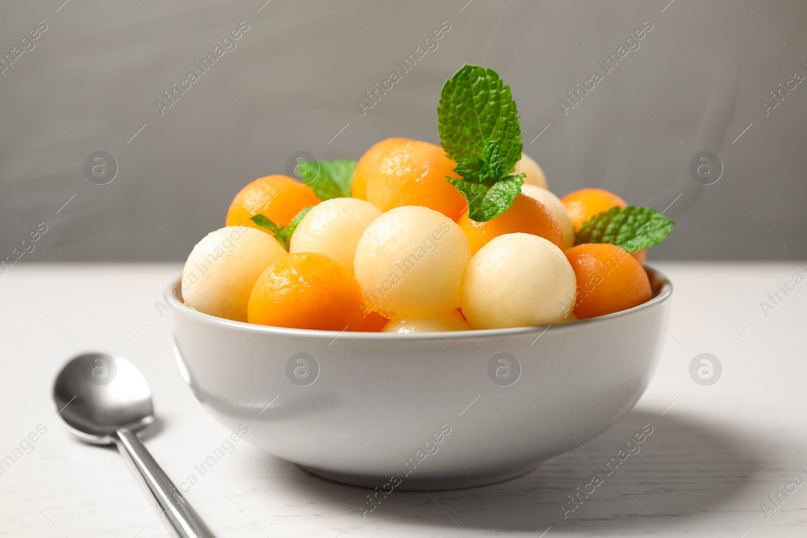 Photo of Melon balls and mint in bowl on white wooden table, closeup