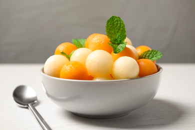 Melon balls and mint in bowl on white wooden table, closeup
