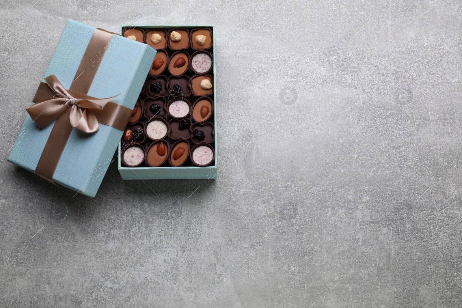 Photo of Open box of delicious chocolate candies on light grey table, top view, Space for text