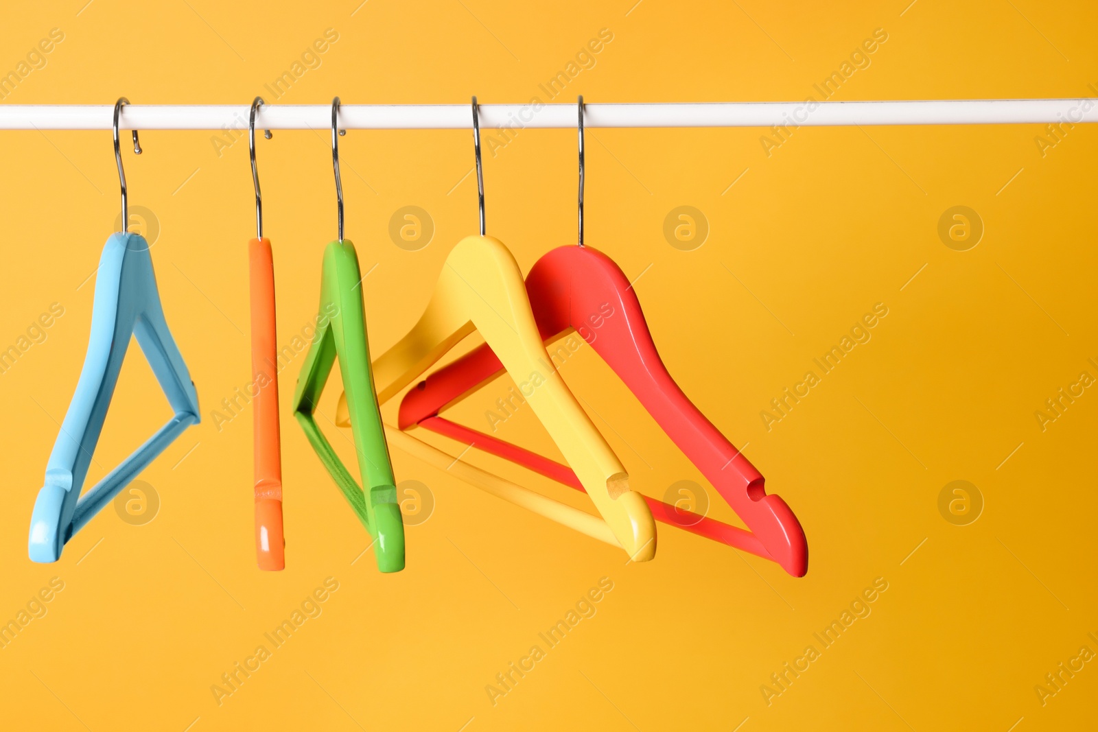 Photo of Bright clothes hangers on metal rail against yellow background