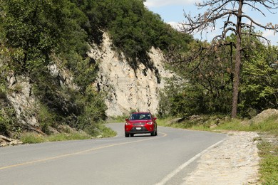 Photo of Red car driving on road near cliff and trees outdoors