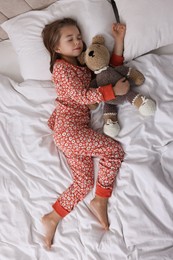 Photo of Cute little girl with toy bear sleeping on bed, top view