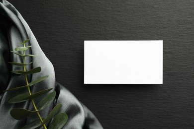 Photo of Blank business card and eucalyptus branch on black background, flat lay. Mockup for design