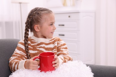 Happy girl with red ceramic mug on sofa at home, space for text