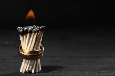 Photo of Burning matches with gold wedding rings on black background, closeup and space for text. Divorce concept