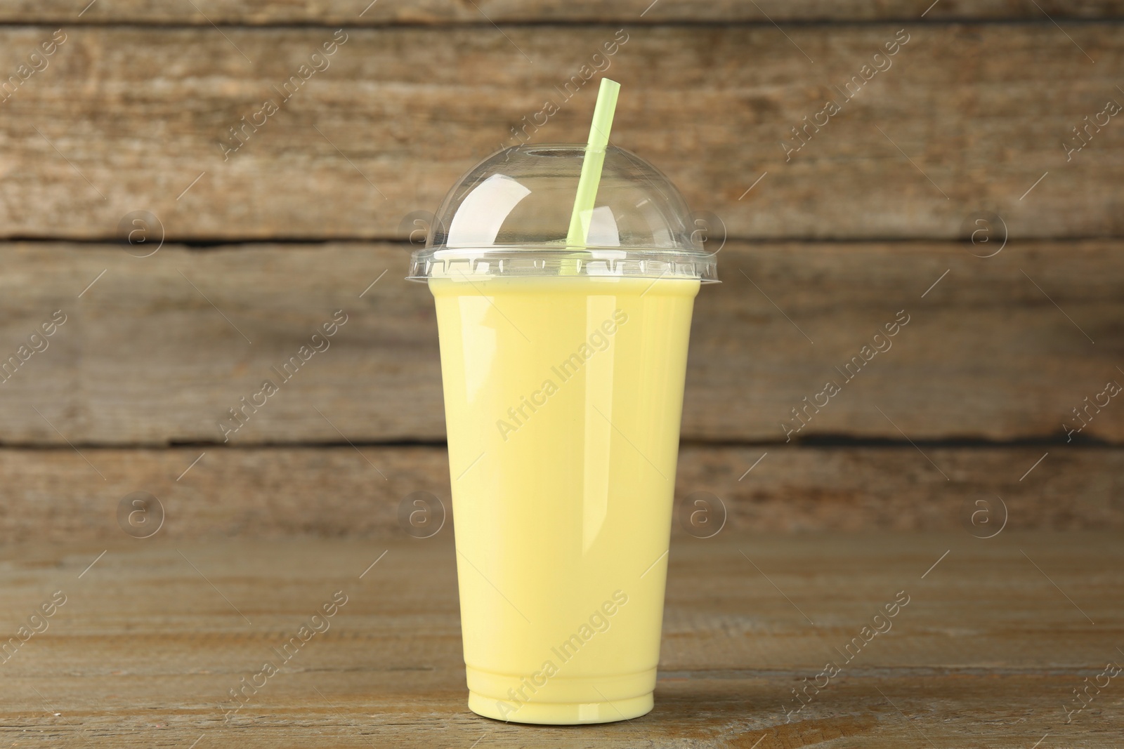 Photo of Plastic cup of tasty smoothie on wooden table