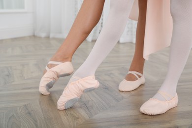Photo of Little ballerina and her teacher practicing dance moves in studio, closeup of legs