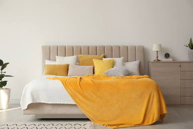 Photo of Stylish bedroom interior with soft yellow pillows and blanket