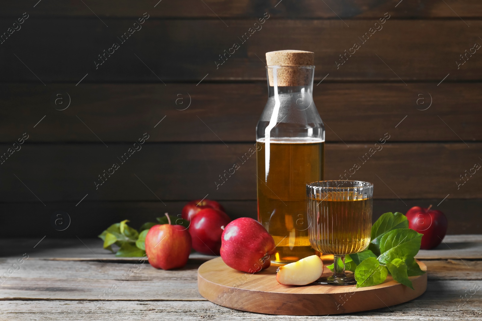 Photo of Delicious cider and apples with green leaves on wooden table, space for text