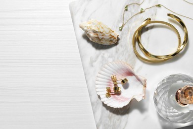 Photo of Different elegant bijouterie, shells and bottle of perfume on white wooden table, top view. Space for text