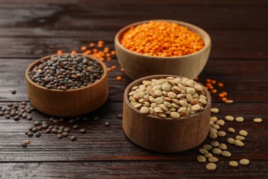 Different types of lentils in bowls on wooden table, closeup