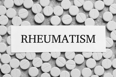 Photo of Card with word Rheumatism and pills on light gray background, flat lay