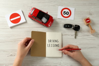 Woman with workbook for driving lessons, car key and road signs at white wooden table, top view. Passing license exam