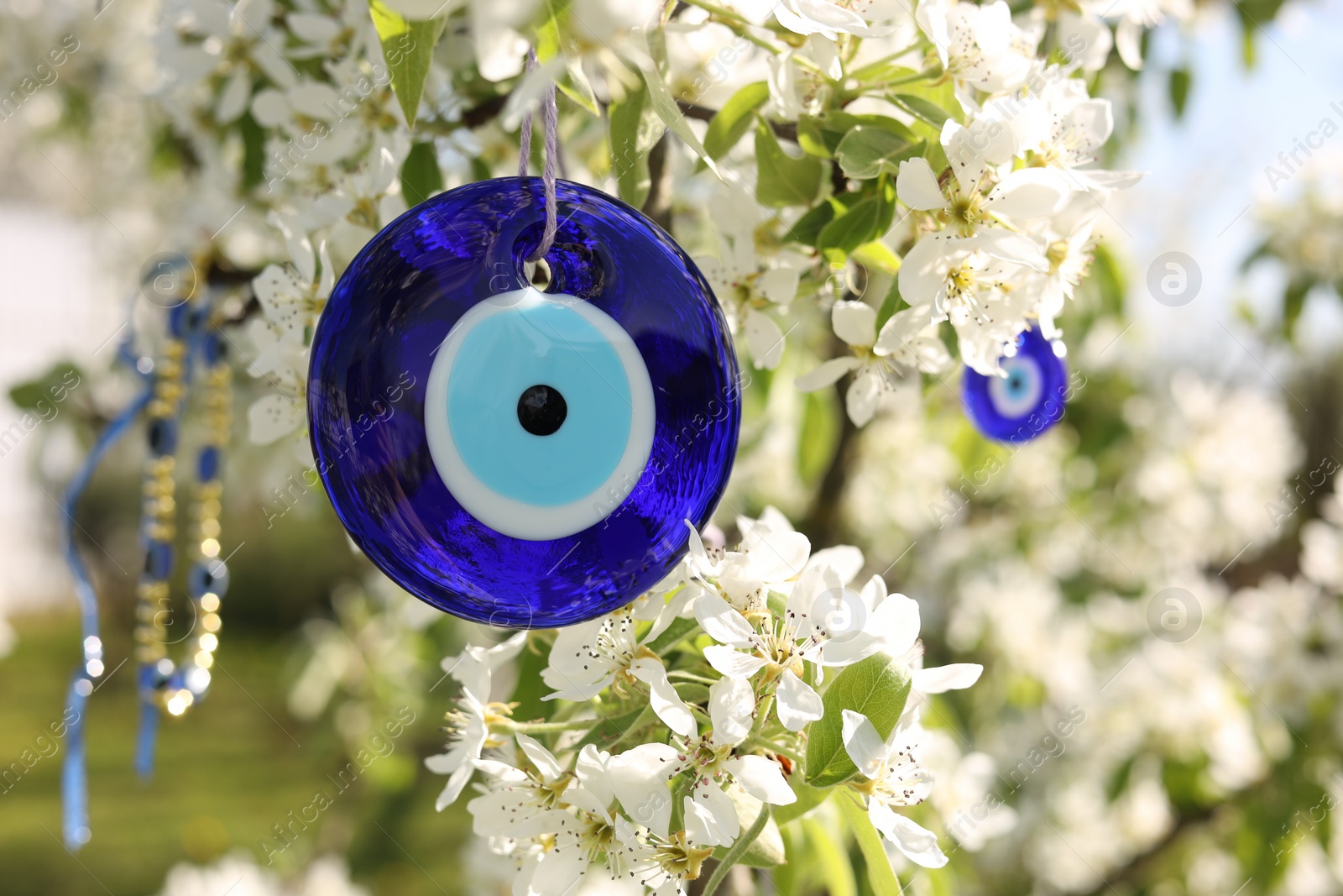 Photo of Eye bead against evil eye hanging on blossoming tree outdoors, closeup